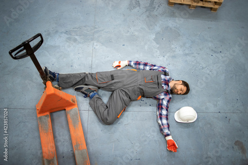 Injury at work. Warehouse worker lying unconscious on the concrete floor after the fall. Safety at work.