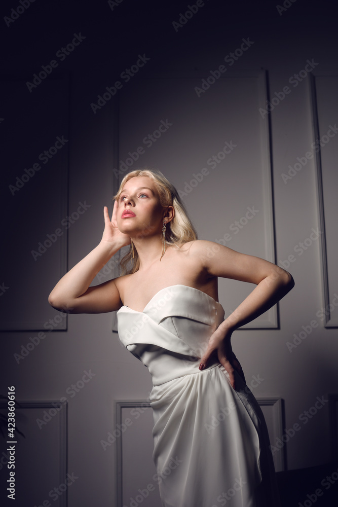 Gorgeous blonde in a white wedding dress. Woman with makeup, styling and silver earrings. The bride is beautiful. Fashion photo ...