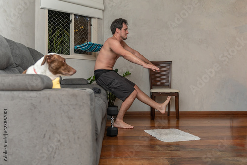 young man exercising at home and the dog is on the sofa