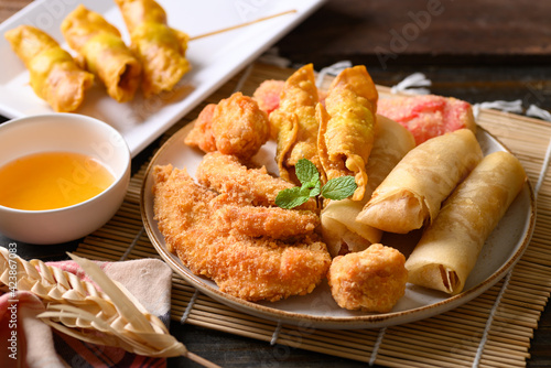 Asian mixed deep fried food (chicken, spring roll, wonton and crab stick) eating with chili sauce on wooden table