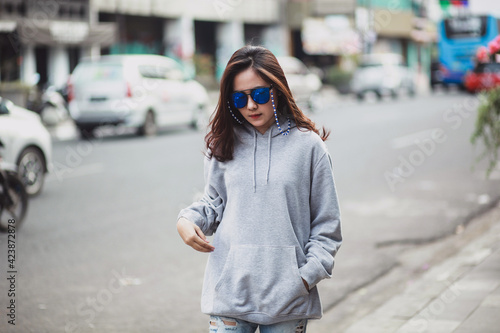 Beautiful woman wearing sweater hoodie and sunglasses walking on the city street