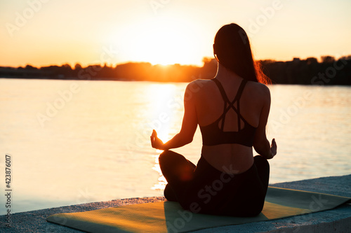 Back view of young woman meditating in sunset , by the river  photo