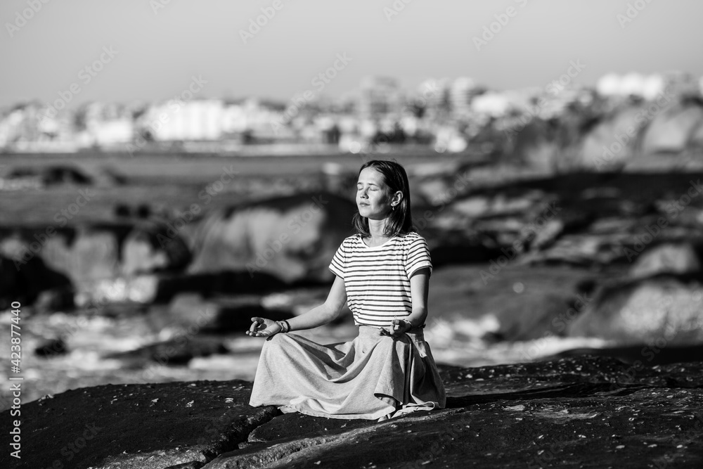 Yoga woman meditating on the rocks on ocean beach. Black and white photo.