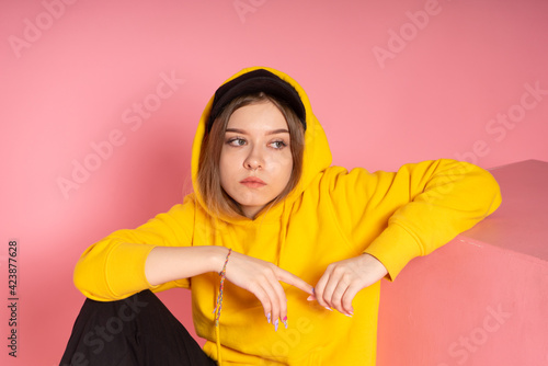 LGBTQ woman in a yellow hoodie sits on pink background © vkfoto