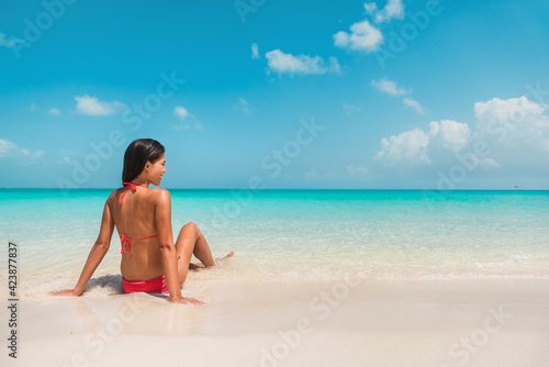Beach travel Caribbean south vacation. Asian bikini woman relaxing sunbathing in water tanning enjoying sun. Winter holidays.
