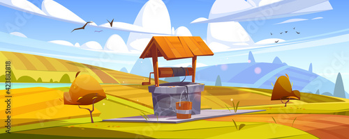 Old stone well with drinking water on yellow hill. Vector cartoon autumn landscape with fields, orange bushes and vintage well with wooden roof, pulley and bucket