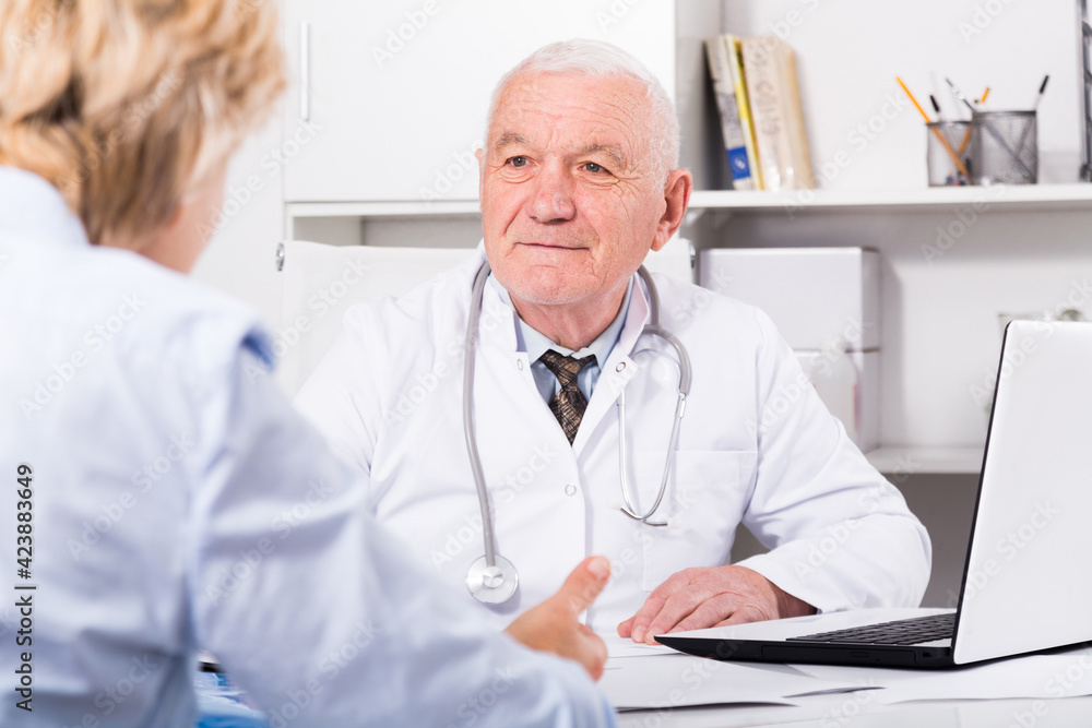 Fototapeta premium Old female visitor consulting smiling aged man doctor in hospital