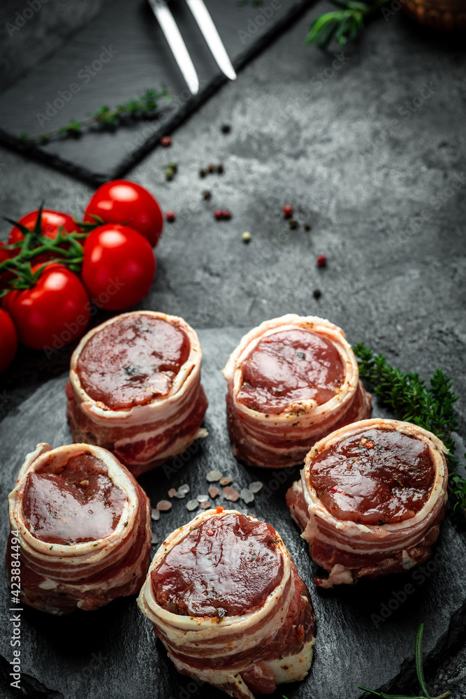Raw steak Tenderloin fillet wrapped in bacon on a dark background, filet Mignon. top view vertical image, place for text Raw steak Tenderloin fillet wrapped in bacon on a dark background, filet Mignon. top view vertical image, place for text