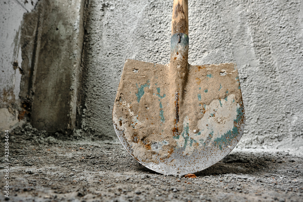 shovel in front of the recently made plastered wall by concrete. green colors exist on metal side of shovel. after construction works. photo taken low angle shovel in front of the recently made plastered wall by concrete. green colors exist on metal side of shovel. after construction works. photo taken low angle
