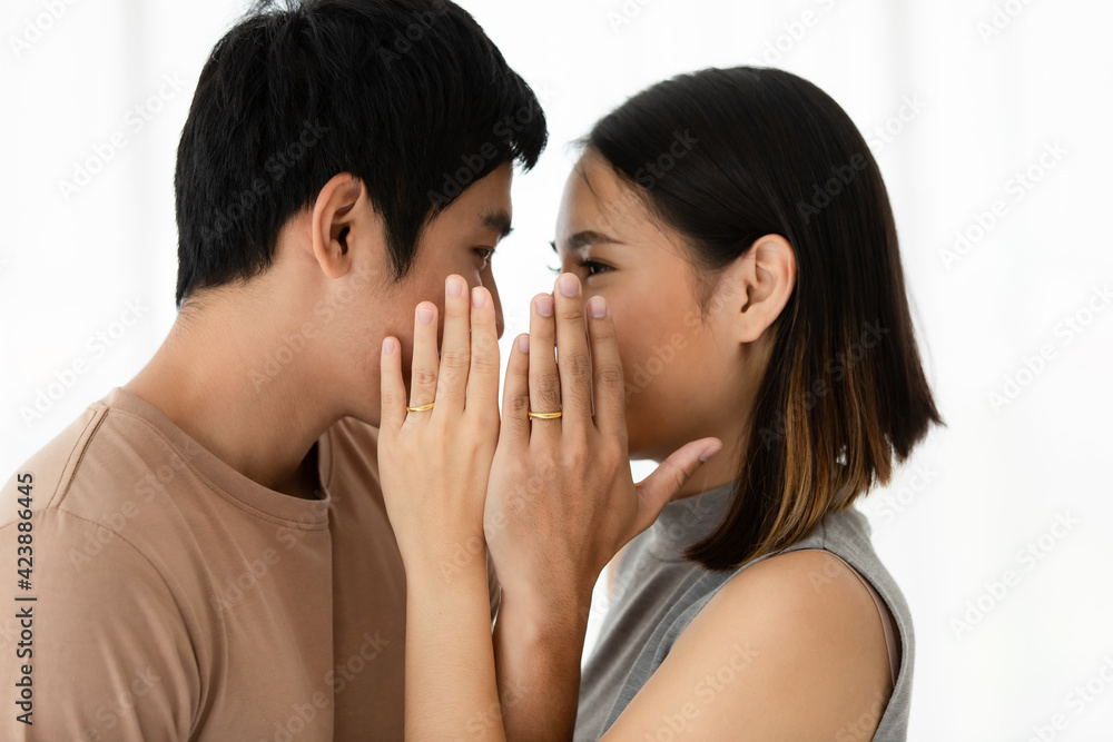 Portrait shot of young Asian lover couple standing closely and looking at each other eyes while showing a golden engagement rings that wore in their ring fingers on white background Portrait shot of young Asian lover couple standing closely and looking at each other eyes while showing a golden engagement rings that wore in their ring fingers on white background