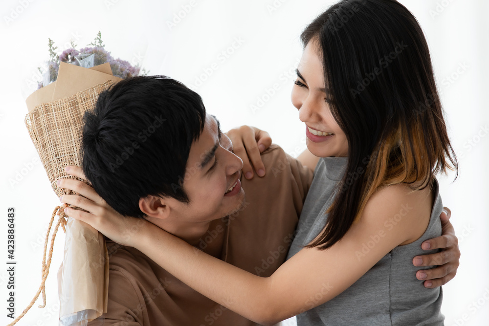 Horizontal portrait shot of cute smiling young Asian lover couple in casual clothes sitting on the bed at home isolated on white background. Husband surprising his wife with a bunch of flowers Horizontal portrait shot of cute smiling young Asian lover couple in casual clothes sitting on the bed at home isolated on white background. Husband surprising his wife with a bunch of flowers