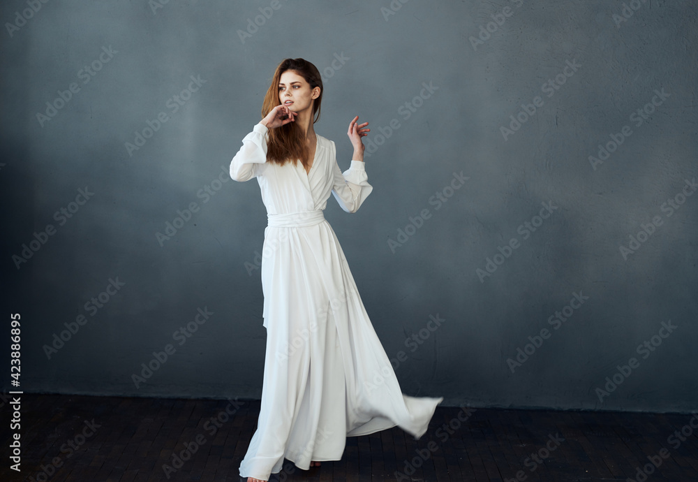Woman on a gray background in a white dress dance model in full growth Woman on a gray background in a white dress dance model in full growth