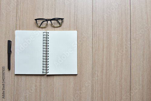 Open notebook with a double page blank space for your text with a fountain pen and glasses on a wooden desk and side copy space