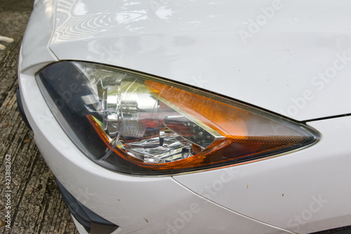 old and crack headlight surface as a result of weather condition and aging of a white car