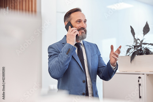 Happy adult caucasian businessman using smarthopne in a modern stylish office