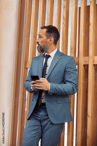 Happy adult caucasian businessman using smarthopne in a modern stylish office