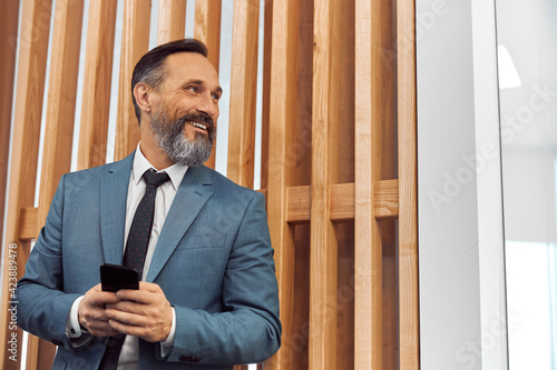 Happy adult caucasian businessman using smarthopne in a modern stylish office