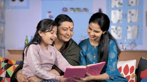 Grandmother with daughter and grandchild reading together sitting on a sofa. A little schoolgirl engaged with a storybook relaxing with her mother and grandmother - family  generation  and people