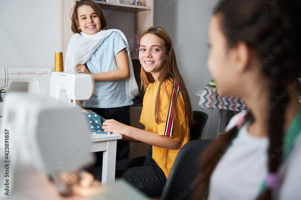 Adorable joyful girls sewing clothes in workshop Adorable joyful girls sewing clothes in workshop
