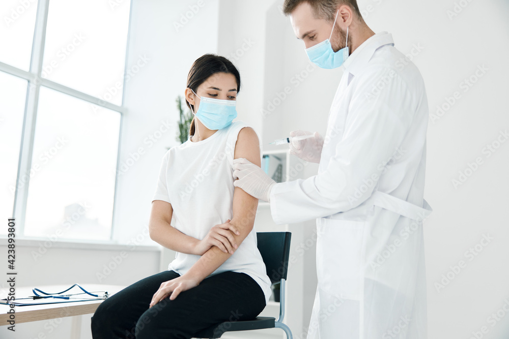 Fototapeta premium a doctor in a medical gown and a mask injects a female patient in the shoulder covid vaccination