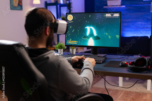 Professional gamer wearing virtual realilty headset and playing space shooter video games with controller. Man streaming online videogames for esport tournament in room with neon lights © DC Studio