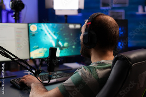 Concentrated gamer playing shooter game for virtual competition using professional headphones. Online streaming cyber performing during gaming tournament using powerful PC with RGB. © DC Studio
