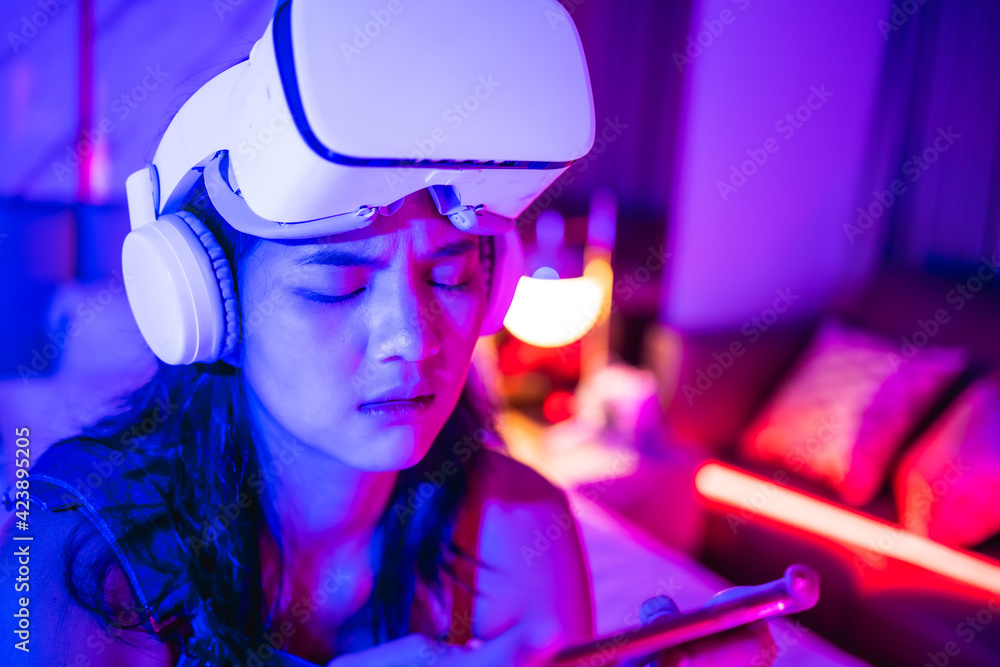 Young asian woman is using virtual reality headset. Neon light studio portrait. Concept of virtual reality, simulation, gaming and future technology.Asian woman play game in bedroom. Young asian woman is using virtual reality headset. Neon light studio portrait. Concept of virtual reality, simulation, gaming and future technology.Asian woman play game in bedroom.