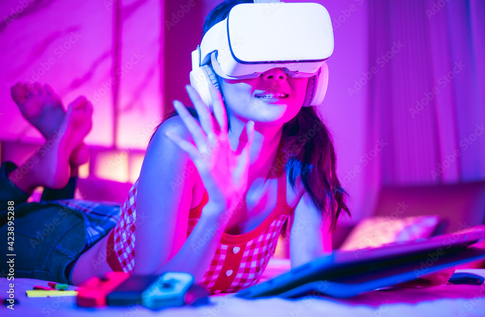 Young asian woman is using virtual reality headset. Neon light studio portrait. Concept of virtual reality, simulation, gaming and future technology.Asian woman play game in bedroom. Young asian woman is using virtual reality headset. Neon light studio portrait. Concept of virtual reality, simulation, gaming and future technology.Asian woman play game in bedroom.