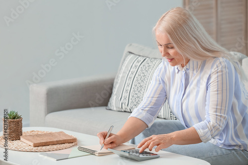 Mature woman with calculator planning her budget at home