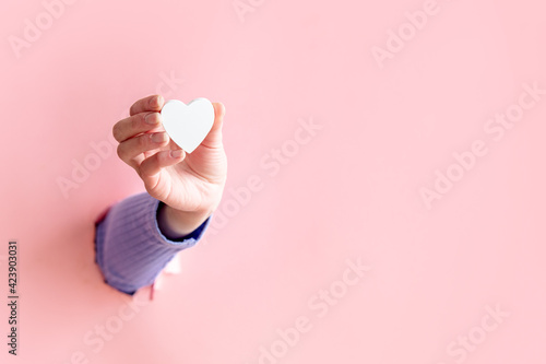 female hand hold little heart on pink background.