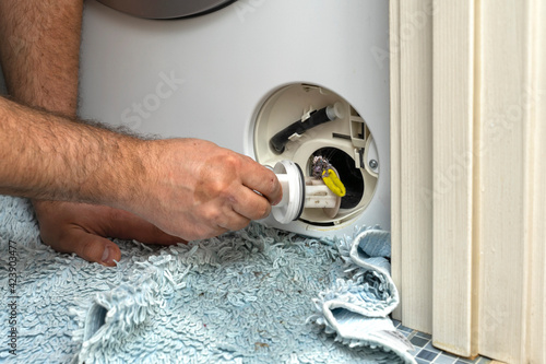 Inspecting washing machine's dirty clogged drain pump filter close up, clean and repair.