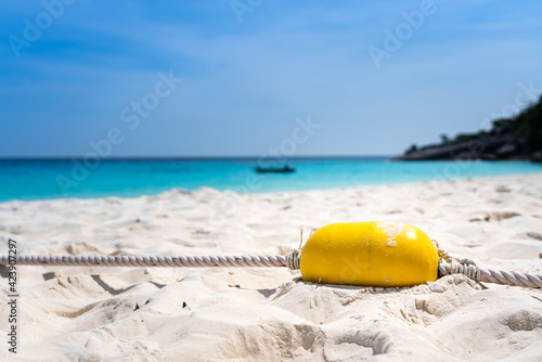 A yellow ocean buoy with rope line is placed on the white beach sand with blurred background of Similan island, Andaman sea in Thailand. The ocean buoy is use to barriace safe area for swimming.