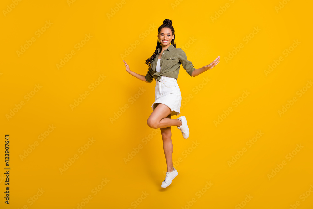 Full body profile photo of carefree dark skin lady jump hands flight wear green white isolated on yellow color background Full body profile photo of carefree dark skin lady jump hands flight wear green white isolated on yellow color background