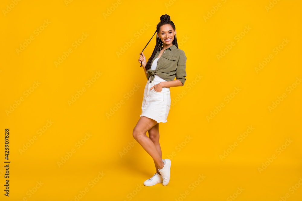 Photo portrait full body view of dark skin girl posing holding hair in hand isolated on vivid yellow colored background Photo portrait full body view of dark skin girl posing holding hair in hand isolated on vivid yellow colored background