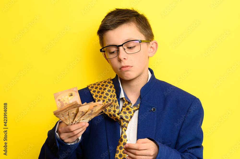 Successful child of successful parents, a boy counts the money earned by parents, a child in an adult suit counts euros. Successful child of successful parents, a boy counts the money earned by parents, a child in an adult suit counts euros.