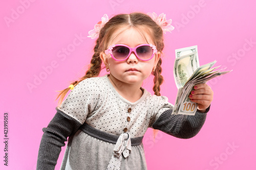 Little girl in glasses with a package and money on a pink background, child and shopping.