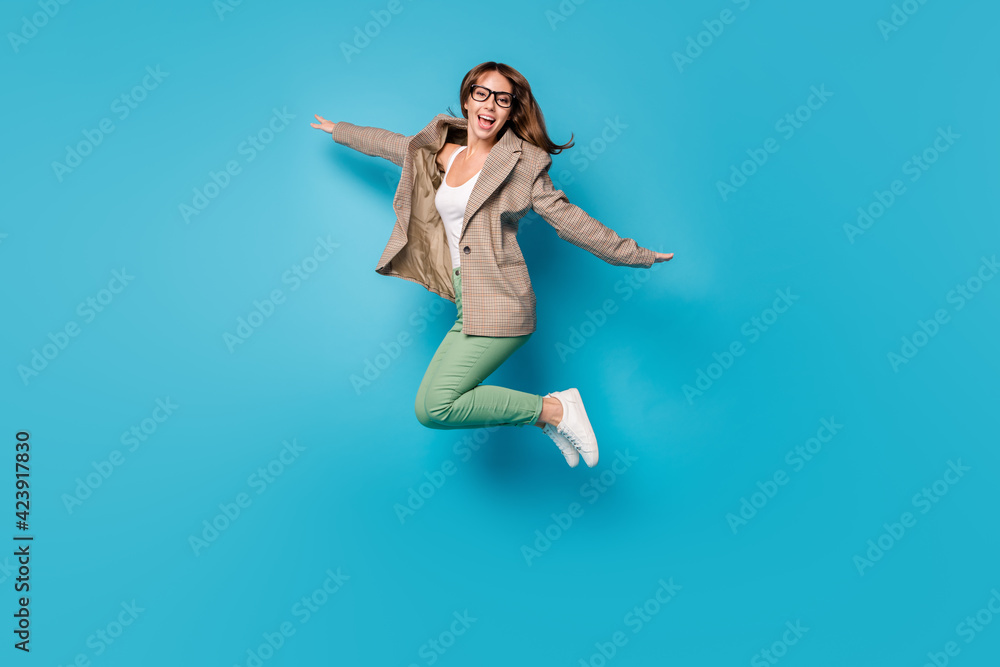 Full length photo portrait of excited girl making plane with hands jumping up isolated on vivid blue colored background