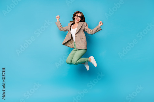 Full length photo of young excited girl happy positive smile rejoice win victory jump fists hands isolated over blue color background