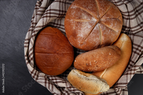 Freshly baked bread loaf bun roll round long mix verity wrapped in checkered kitchen fabric napkin towel over black background photo