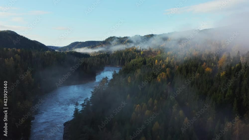 Aerial view over a river, hills and foliage forest, foggy, fall morning, in South Norway - rising, drone shot Aerial view over a river, hills and foliage forest, foggy, fall morning, in South Norway - rising, drone shot