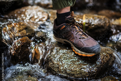 a foot in a brown trekking boot stands on a wet rock in a mountain river