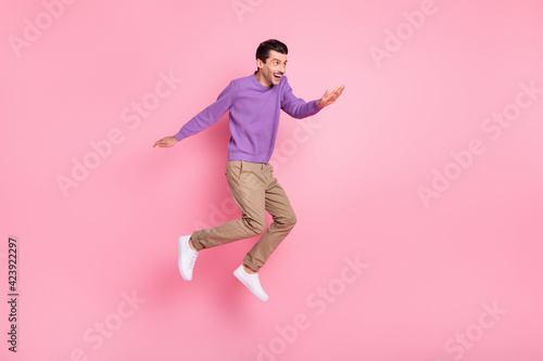 Photo of positive cute young guy wear violet sweater jumping high looking empty space isolated pink color background