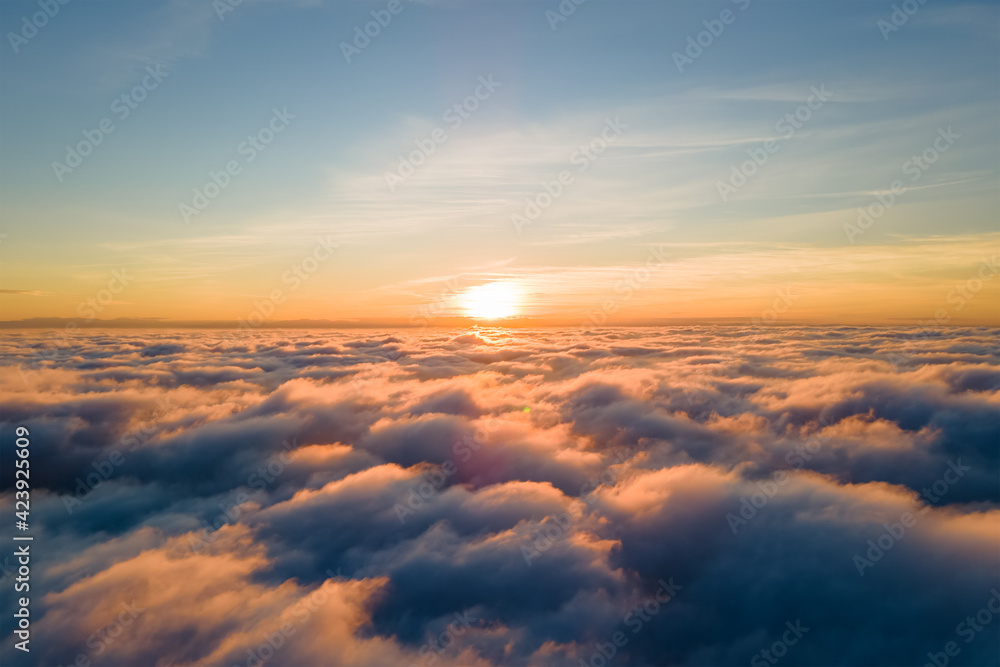 Aerial view of bright yellow sunset over white dense clouds with blue sky overhead. Aerial view of bright yellow sunset over white dense clouds with blue sky overhead.