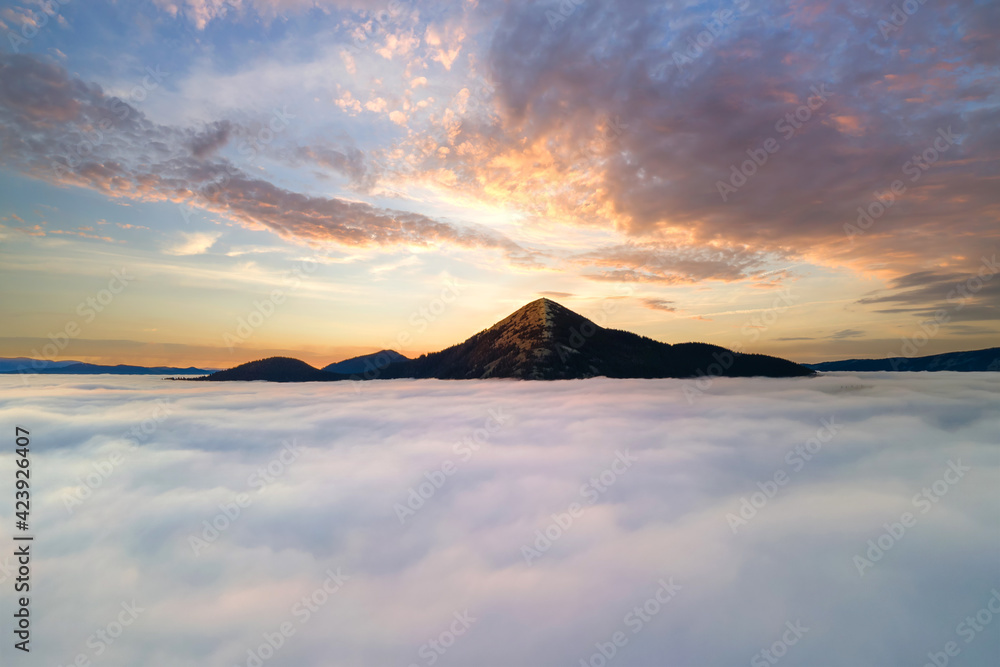 Aerial view of vibrant yellow sunrise over white dense clouds and distant mountains on horizon.