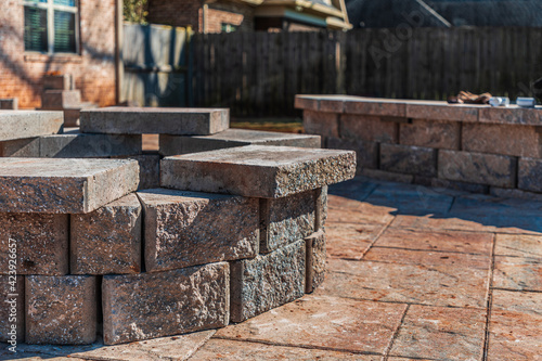 Incomplete paver patio hardscape with a stone fire pit and seating wall under construction in a fenced suburban backyard
