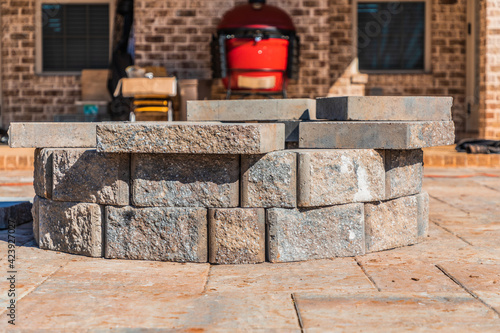 Incomplete paver patio hardscape with a fire pit feature under construction in a suburban backyard