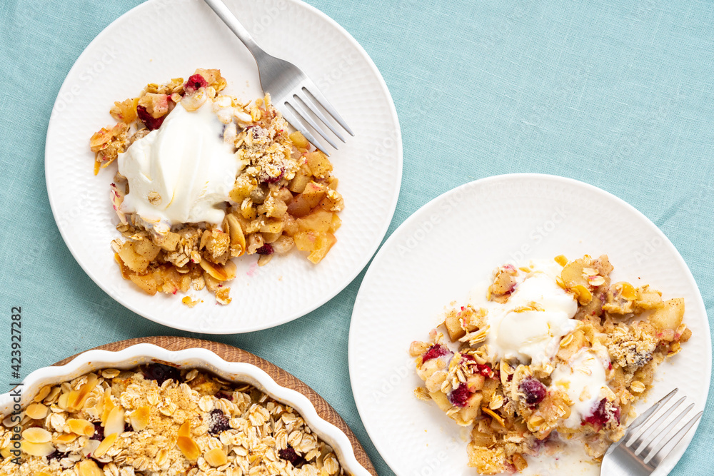 Two plate with apple pear crumble with ice cream, streusel. Sweet dessert with stewed fruit topped crisp crumbly mixture served ice cream. Apple cobbler pie in baking dish on tablecloth. Top view Two plate with apple pear crumble with ice cream, streusel. Sweet dessert with stewed fruit topped crisp crumbly mixture served ice cream. Apple cobbler pie in baking dish on tablecloth. Top view