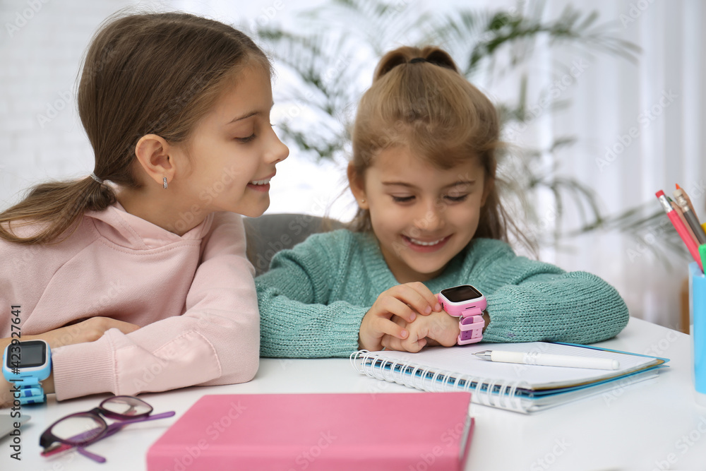 Girls with stylish smart watches at table indoors Girls with stylish smart watches at table indoors