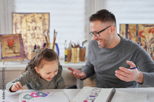 Happy attractive caucasian family creative art hobby and funny tome spending. Caring dad or babysitter drawing with colored pencils teaching child girl sitting at the table. High quality photo