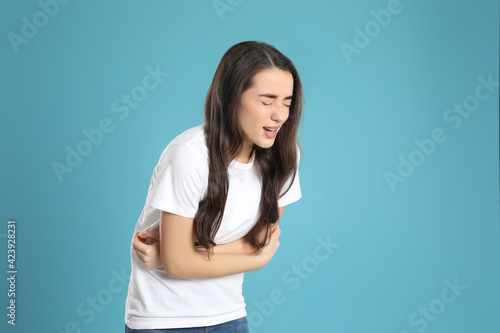 Young woman suffering from stomach ache on light blue background. Food poisoning photo